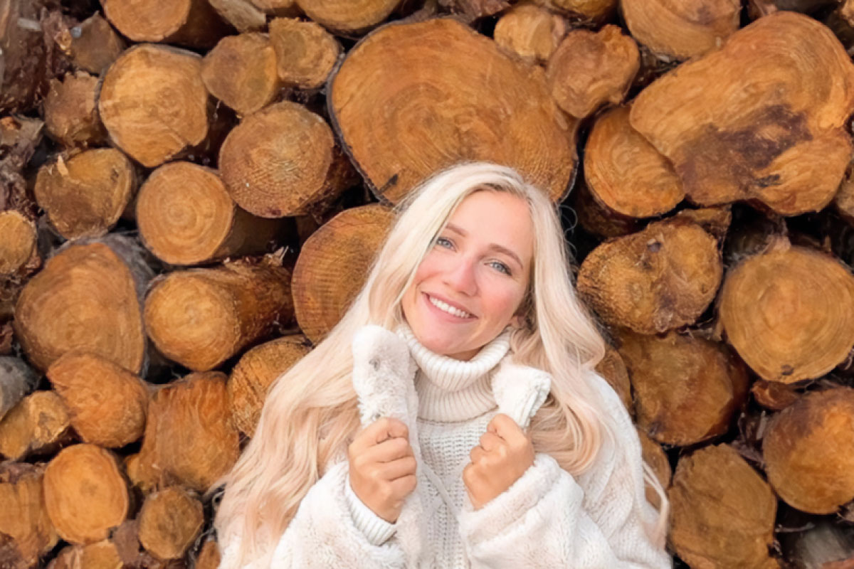 Junge Frau in weißem Pullover vor Holzstapeln, Bild von Lena Schiwiora für Rezension zur Arkona Sky Bar auf Rügen.