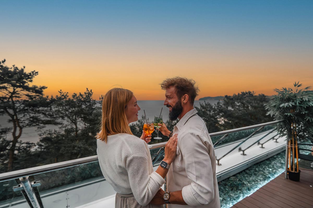 Paar stößt bei Sonnenuntergang mit Cocktails in der Sky Bar in Binz mit Blick auf die Ostsee an.