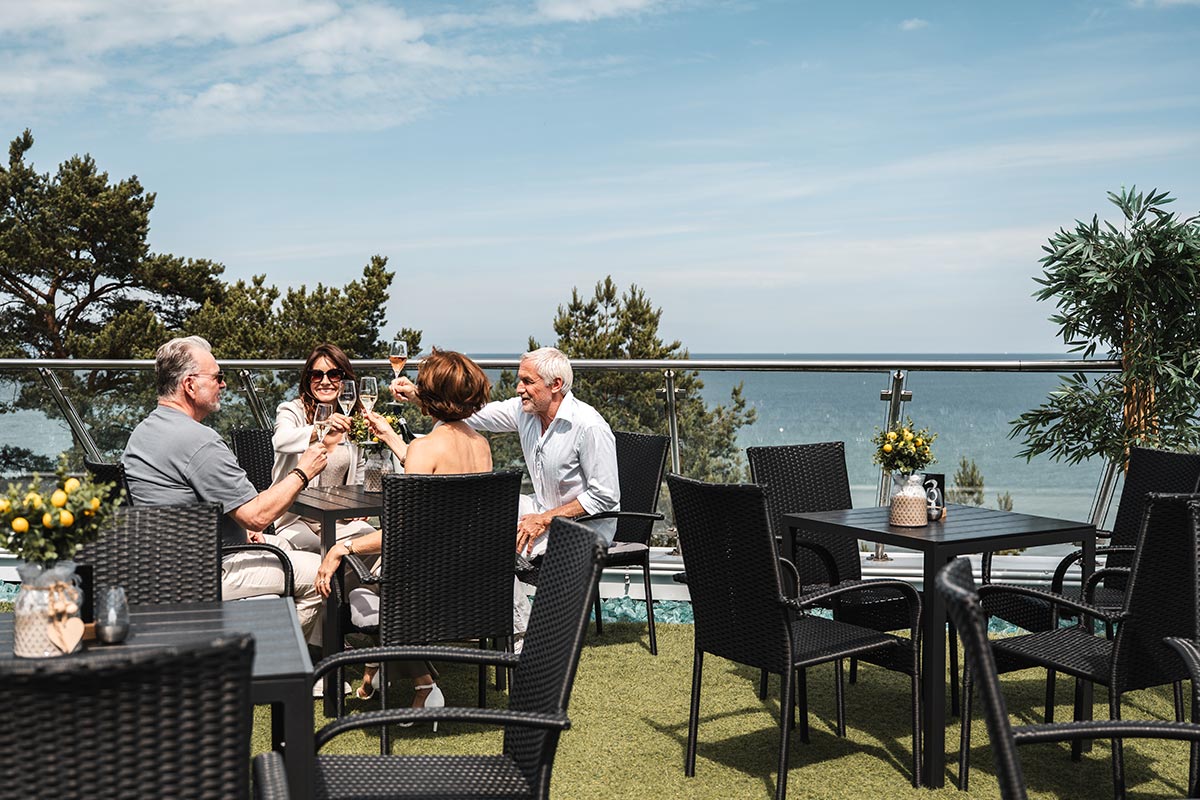 Vier Personen stoßen an einem Tisch der Sky Bar in Binz mit Blick auf die Ostsee an.