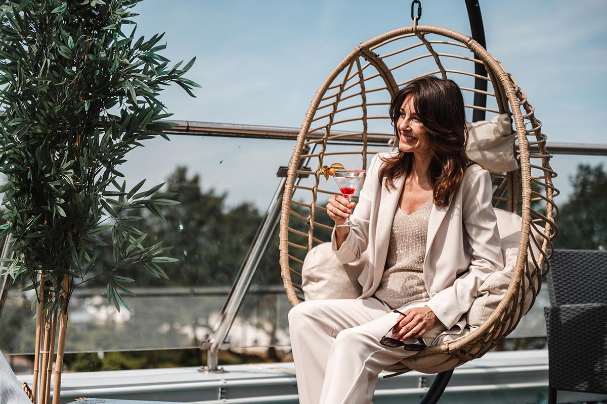 Frau sitzt mit einem Cocktail im Hängesessel auf der Terrasse der Sky Bar in Binz.
