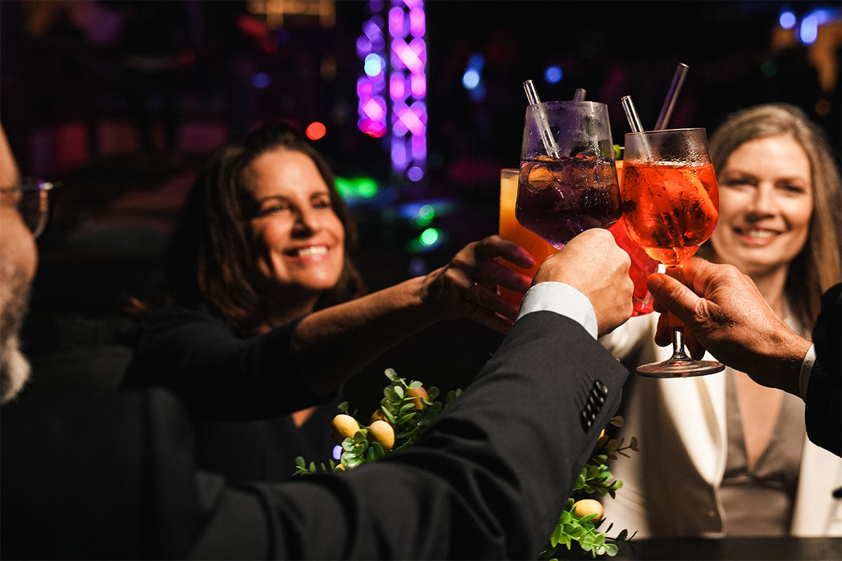 Vier Gäste stoßen in der Sky Bar Binz mit bunten Cocktails an, im Hintergrund farbige Lichter