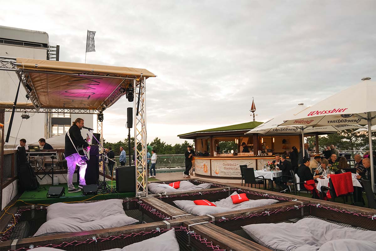 Musiker mit Gitarre auf der Bühne der Sky Bar Binz, davor Netzliegen mit Kissen, rechts Gäste an Tischen und die Cocktailbar