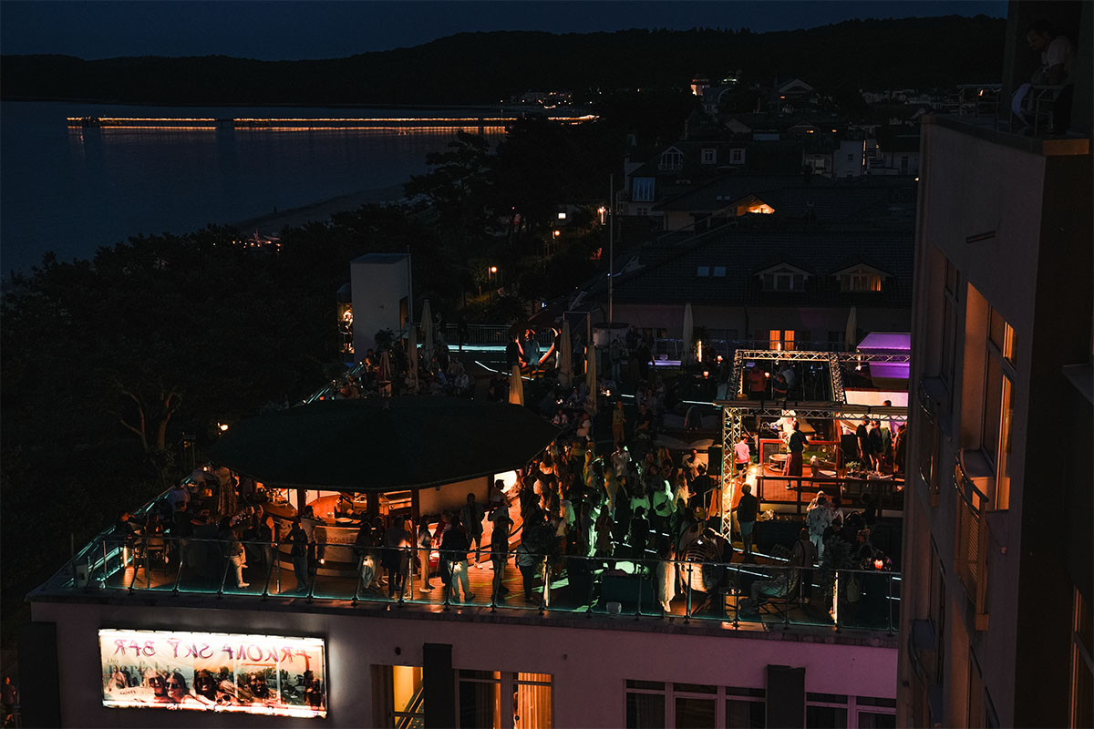 Nächtliche Feier auf der Dachterrasse der Sky Bar Binz mit vielen Gästen, im Hintergrund die beleuchtete Seebrücke Binz und die Ostsee