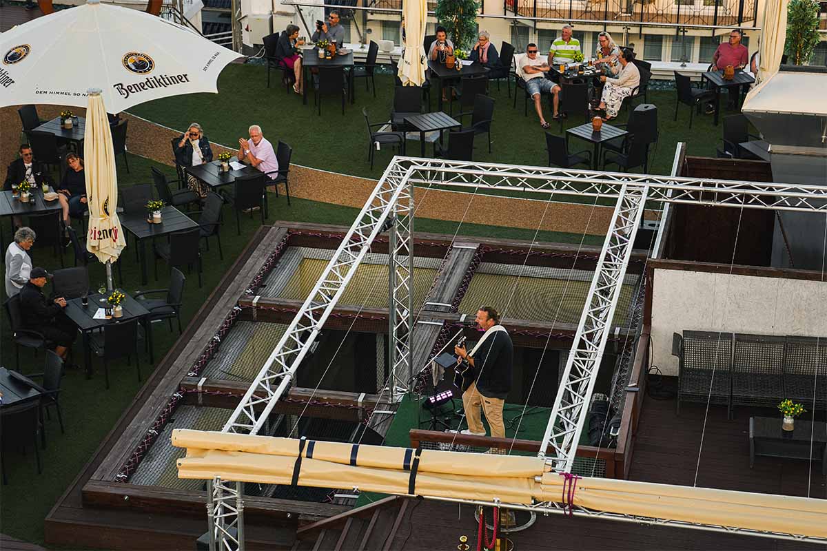 Blick von oben auf die Dachterrasse der Sky Bar Binz mit Gitarrist auf der Bühne zwischen Netzliegen und Gästen an Tischen