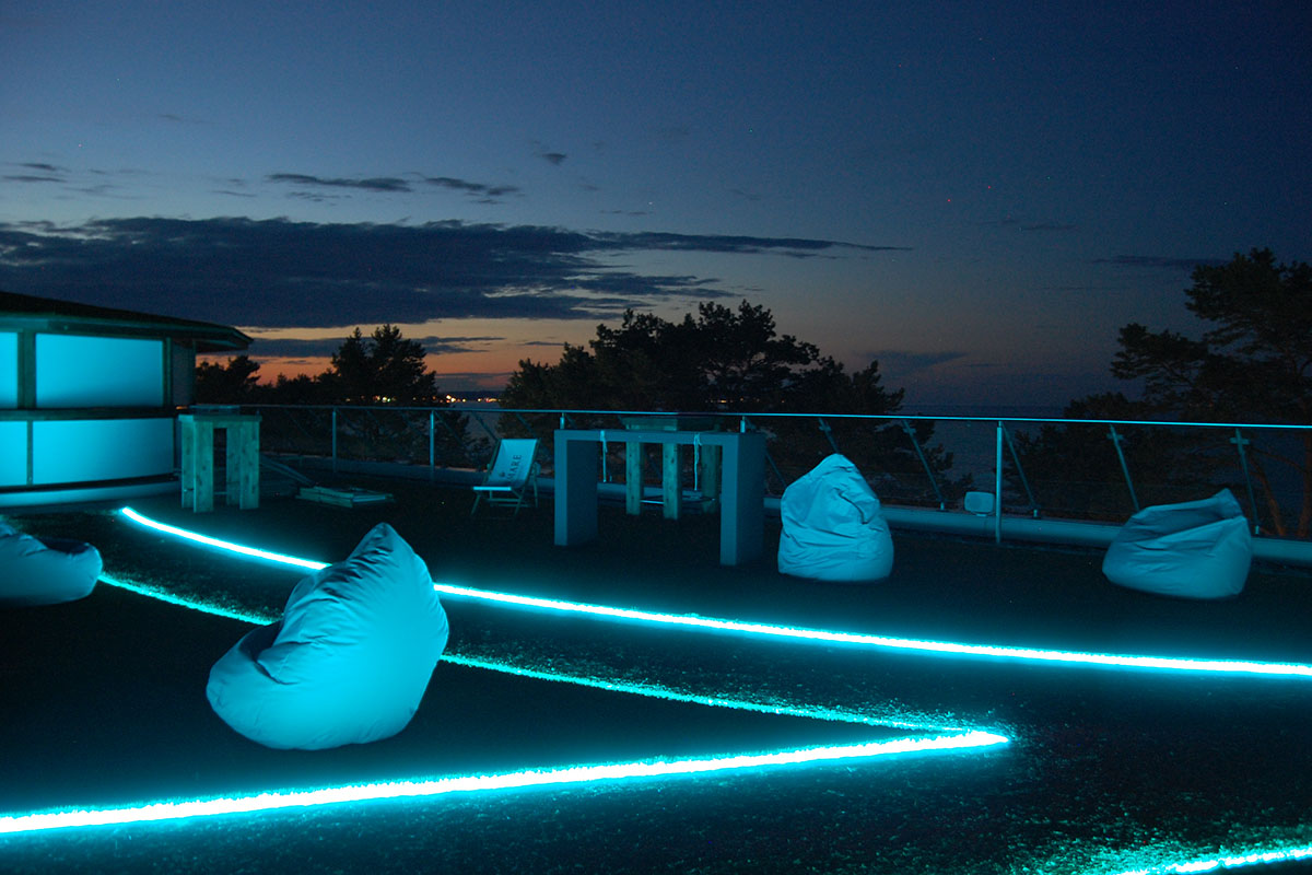 Terrasse mit Lichtlinien, Sitzsäcken und Hochtischen auf dem Dach der Arkona Sky Bar auf Rügen bei Nacht.